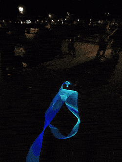 A ribbon of Trippy Wire spun through the air at night, shifting blue to cyan.